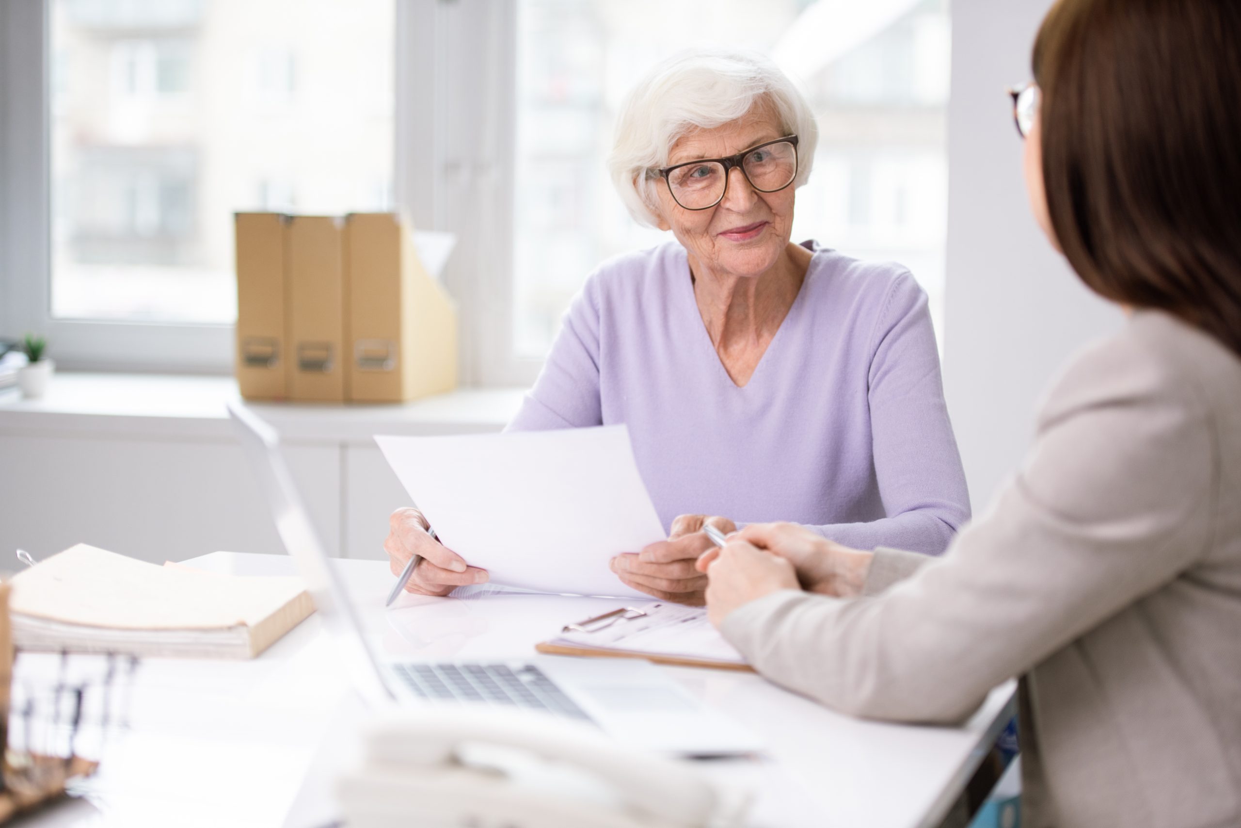 Content white-haired lady in glasses sitting at table and counseling on document issues with social worker